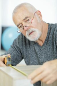senior man provides help with furniture by measuring desk to be moved